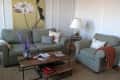 Living room with green sofa, armchair, floral artwork, wooden coffee table, and lavender vase.