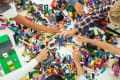 Children's hands reaching for colorful LEGO bricks scattered on a table.