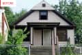 Small beige house with brown trim, front porch, and metal gate, surrounded by greenery.