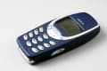 Classic Nokia 3310 mobile phone with blue casing and white buttons on a light surface.