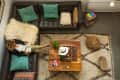 Cozy living room with a brown leather sectional, colorful pillows, wooden coffee table, and a person reading a book.