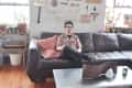 Man sitting on a dark leather sofa in a loft with eclectic wall decor and a wooden floor.