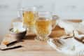 Two glass mugs of herbal tea on a wooden countertop with a tea bag and cloth napkin nearby.