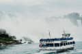 Boat full of tourists in blue ponchos near Niagara Falls, surrounded by mist and cascading water.