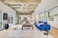 Open-concept living room with blue sofa, wooden coffee table, white rug, and modern decor under exposed beam ceiling.