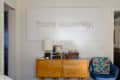 Bedroom with wooden dresser, blue chair, colorful mobile, and "Yours sincerely," wall art above.