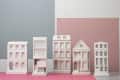 Five white architectural model buildings on a pink surface with blue and pink panels in the background.