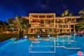 Modern luxury mansion with illuminated geometric design, large pool, and surrounding trees at night.