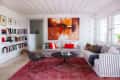 Living room with striped sofas, red cushions, abstract painting, bookshelves, and a black wire chair on a red rug.