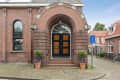 Arched brick entrance with black and wood door, potted plants, and a dead-end street sign.