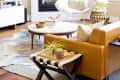 Modern living room with tan leather sofa, round coffee table, fireplace, and large window with natural light.