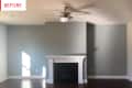 Empty living room with gray walls, white fireplace, ceiling fan, and hardwood floors.
