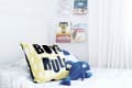 Child's bed with "Boys Rule" pillow, blue plush toy, and books on wall shelves.