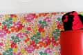 Yellow flower chandelier with green leaves above a colorful floral wallpaper and red cylindrical object.