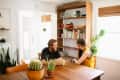 Couple sitting at a wooden table with potted cacti, surrounded by bookshelves and plants in a bright room.