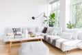 Modern living room with white sectional sofa, decorative pillows, wooden coffee table, books, plants, and large windows.