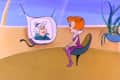 Woman in purple dress sitting in futuristic room, talking to another woman on a screen.