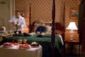 Boy sitting on a four-poster bed in a vintage room with a waiter serving food and a table with desserts.