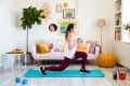 Woman doing lunges on a blue mat in a colorful living room with a sofa, plants, and wall art.