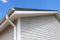 House roof corner with white siding, gutter, and downspout against a clear blue sky.