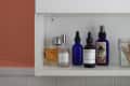 Bathroom shelf with various skincare bottles, a glass jar with cotton swabs, and floral-patterned towels hanging below.