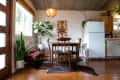 Dining area with wooden table and chairs, plants, pendant light, and white fridge in a cozy kitchen setting.
