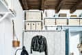 Cozy room with wooden ceiling, leather jacket on lace curtain, potted fern, and storage boxes on shelves.