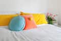 Bed with yellow polka dot pillows, blue and orange cushions, and pink tulips in a vase on a white nightstand.