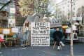 Outdoor scene with two people offering free furniture, lamps, and decor items on a sidewalk.