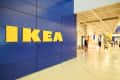 IKEA store entrance with blue wall and yellow logo, people walking inside, and visible escalator.