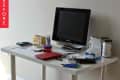 Cluttered white desk with a monitor, scattered papers, notebooks, and various office supplies.
