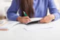 Person in blue sweater writing on a black envelope at a white desk with scattered papers.