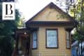 Yellow house with brown trim, front porch, and large windows, surrounded by trees.