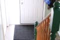 Entryway with white door, black mat, wooden staircase, and coats hanging on the wall.