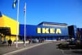 IKEA store exterior with blue and yellow facade, flags, and people entering.
