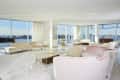 Spacious living room with large windows, cream sofas, a grand piano, and a view of the city skyline.