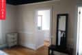 Empty room with beige walls, wooden floor, white dresser, and a tall mirror next to a doorway leading to a bathroom.