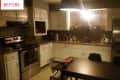 Dimly lit kitchen with white cabinets, stainless steel appliances, and a dark dining table.