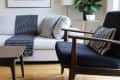 Modern living room with a white sofa, black armchair, abstract art, and a potted plant on a wooden floor.