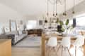 Open-plan living and dining area with gray and brown sofas, wooden table, white chairs, bookshelves, and hanging lights.