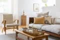 Modern living room with a beige armchair, gray sofa, patterned cushions, wooden coffee table, and decorative plants.
