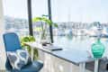Home office with blue chair, desk, laptop, plant, and marina view through large windows.