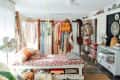 Bohemian bedroom with floral bedspread, hanging plants, vintage fans, and a room divider displaying clothes and bags.