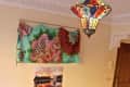Colorful living room with a blue sofa, vibrant cushions, patterned wall hanging, mosaic lamp, and a table with flowers.