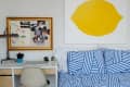 Bedroom with blue and white striped bedding, desk with chair, framed photos, and large yellow lemon artwork on the wall.