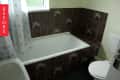 Bathroom with brown floral tiles, white bathtub, floral shower curtain, and toilet.