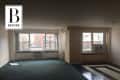 Empty living room with large windows, green carpet, and striped flooring, overlooking city buildings.