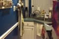 Narrow kitchen with blue walls, spice rack, hanging pots, and a small sink area with dish rack and utensils.