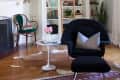 Living room with a black armchair, white side table, ladder bookshelf, chandelier, and decorative items.