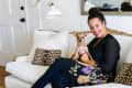 Woman sitting on a white sofa with a small dog, leopard print pillows, and a wall lamp.